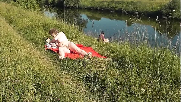 Hotte MILF sexy Frina on river bank undressed and sunbathes naked. Random man fisherman watching for her, and in the end decided to join naked woman. Wild beach. Nudist beach. Public nudity. Public exposure. Naked in public varme filmer
